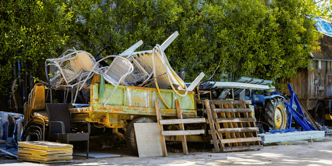 A bin outside on a sunny day in front of green foliage full of discarded clutter showing an example of what Ebb & Spruce can help you let go of. 